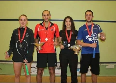 Photo of four squash players with medals on thier necks.