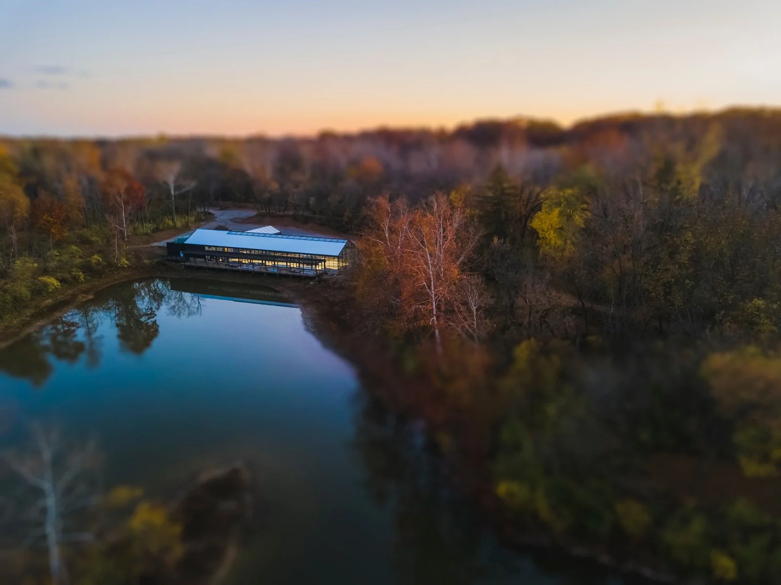 a gorgeous all-glass conservatory sits nestled among fall foliage and sits on a private lake