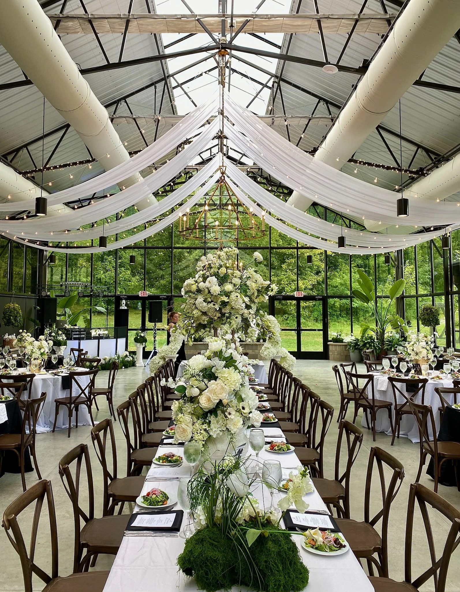 Elegant indoor wedding reception setup with long head table decorated with white floral centerpieces at The Conservatory at Evergreen.