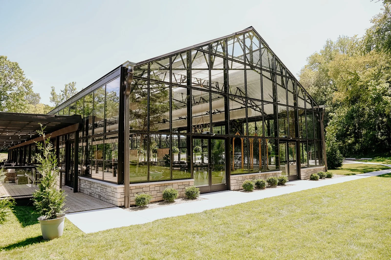 The all-glass Conservatory at Evergreen, surrounded by Indy's best nature, under clear sky.