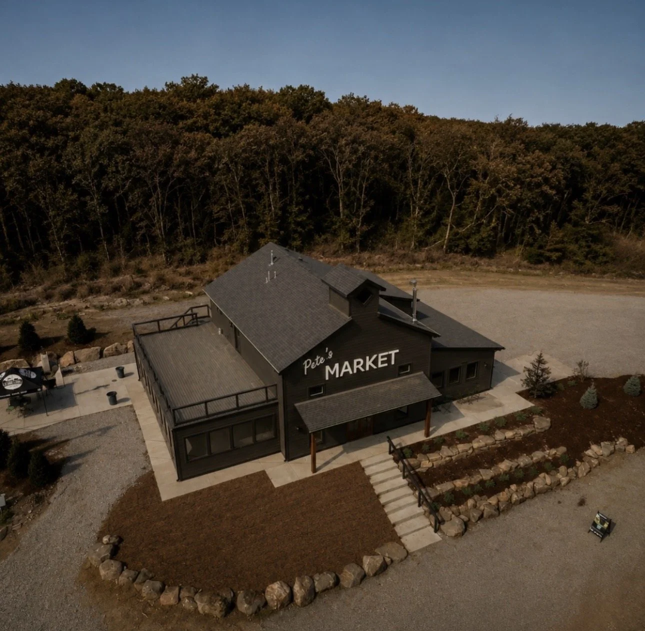 Aerial view of a black building labeled 'Pete's Market' with a large parking lot and surrounding trees.