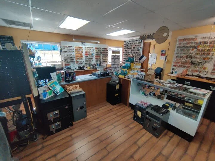 Interior of a small store with various keys, locks and locksmith accessories displayed on wall-mounted racks, a glass display case, and counters with items for sale.