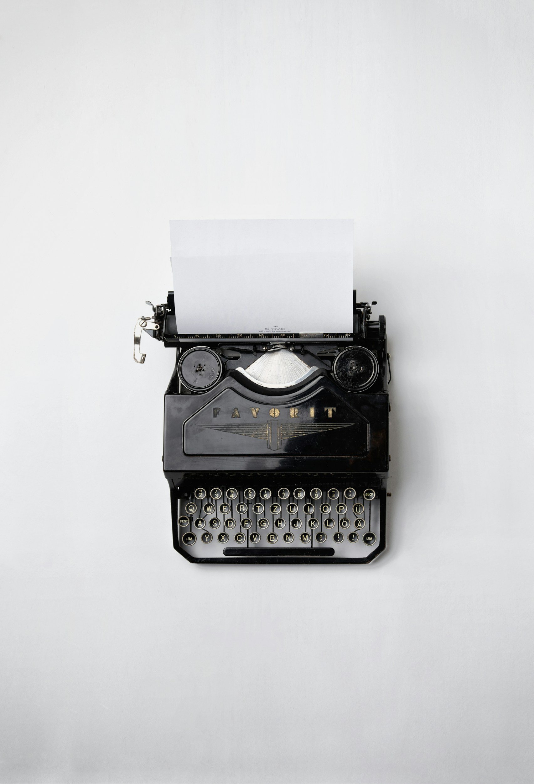 An antique black typewriter with round keys and faded gold branding on a white background.