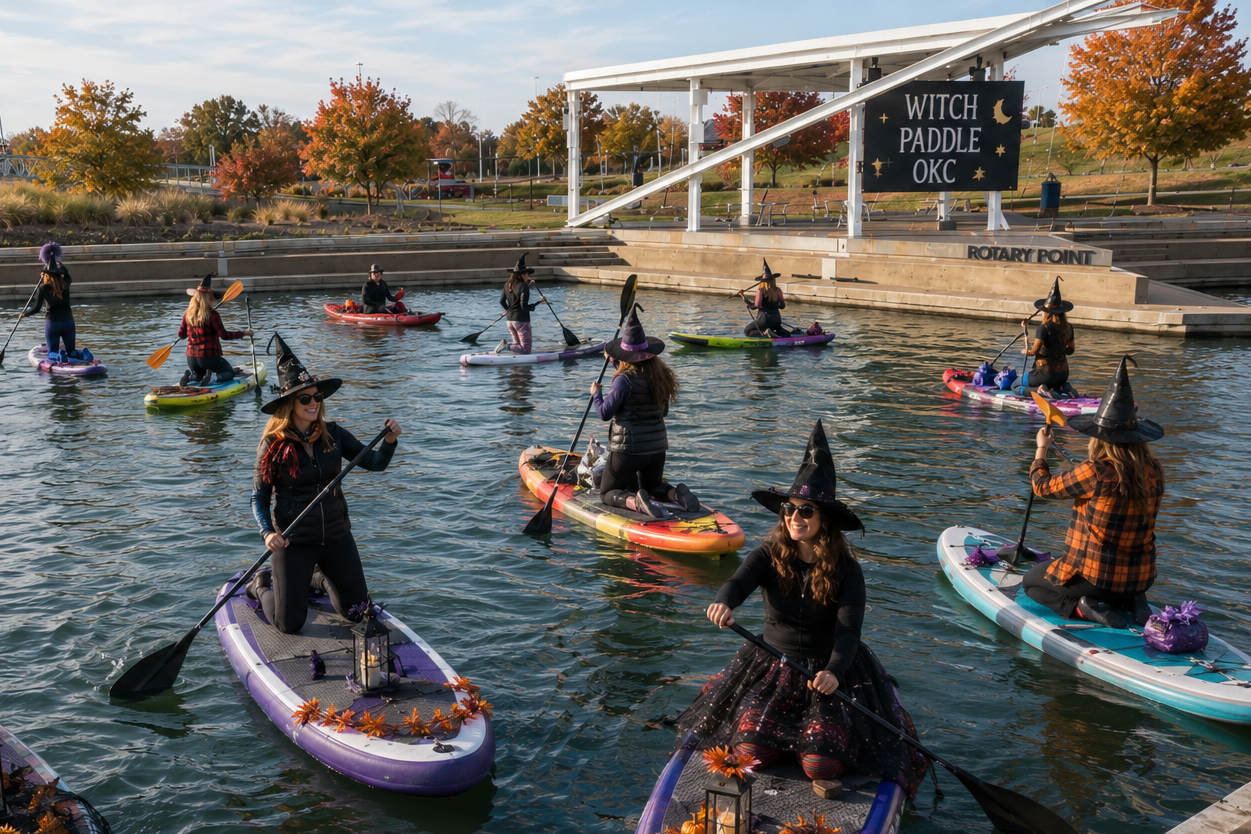 Group of women dressed as witches paddleboarding at Riversport during a Halloween event, with a sign that reads 'Witch Paddle OKC' and autumn trees in the background.