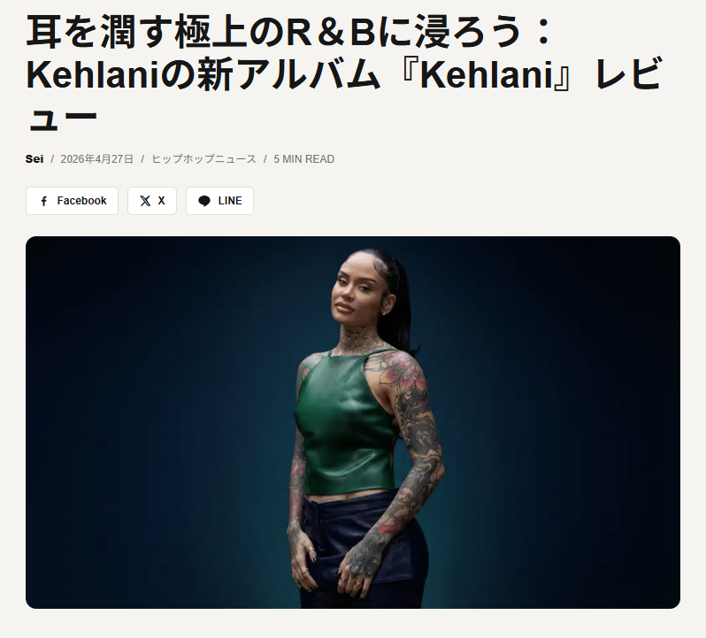A woman with tattoos on her arms and neck, wearing a sleeveless green top and dark pants, standing against a dark background.
