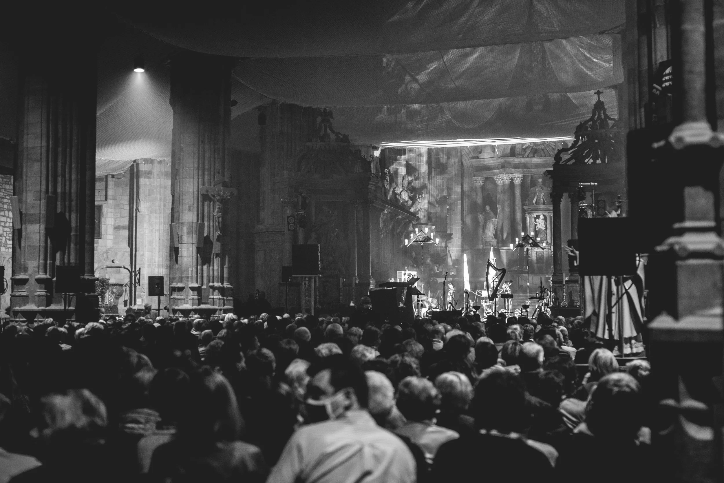 Intérieur d'une grande cathédrale avec un public assis, préparation pour un concert ou une performance, avec une scène équipée de microphones et instruments, scènes d'architecture gothique avec statues et colonnes.