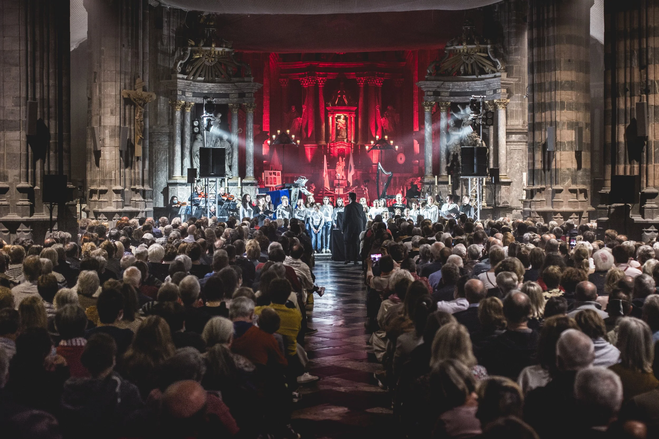 Chorale en concert dans une ancienne église avec un fond d'autel monumental en arrière-plan, et un public nombreux dans la nef.