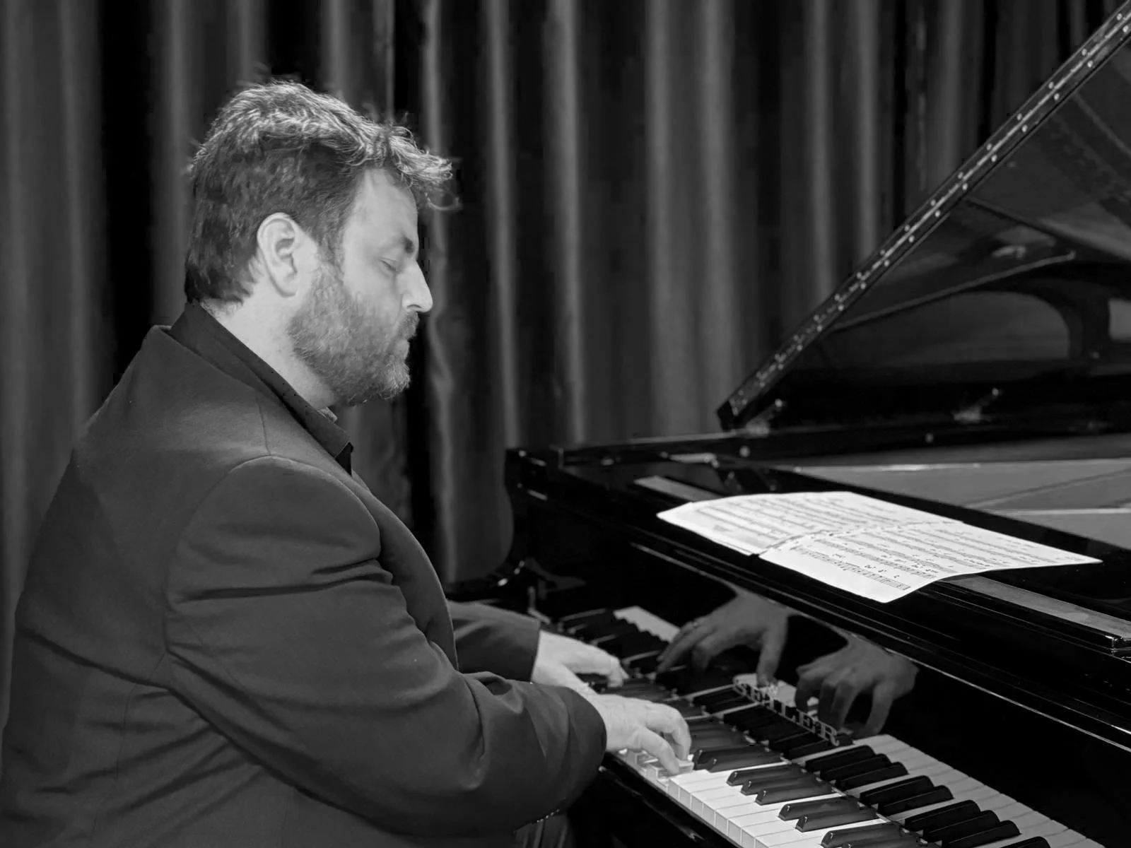 Un homme avec des cheveux et une barbe joue du piano, yeux fermés, lors d'une performance.