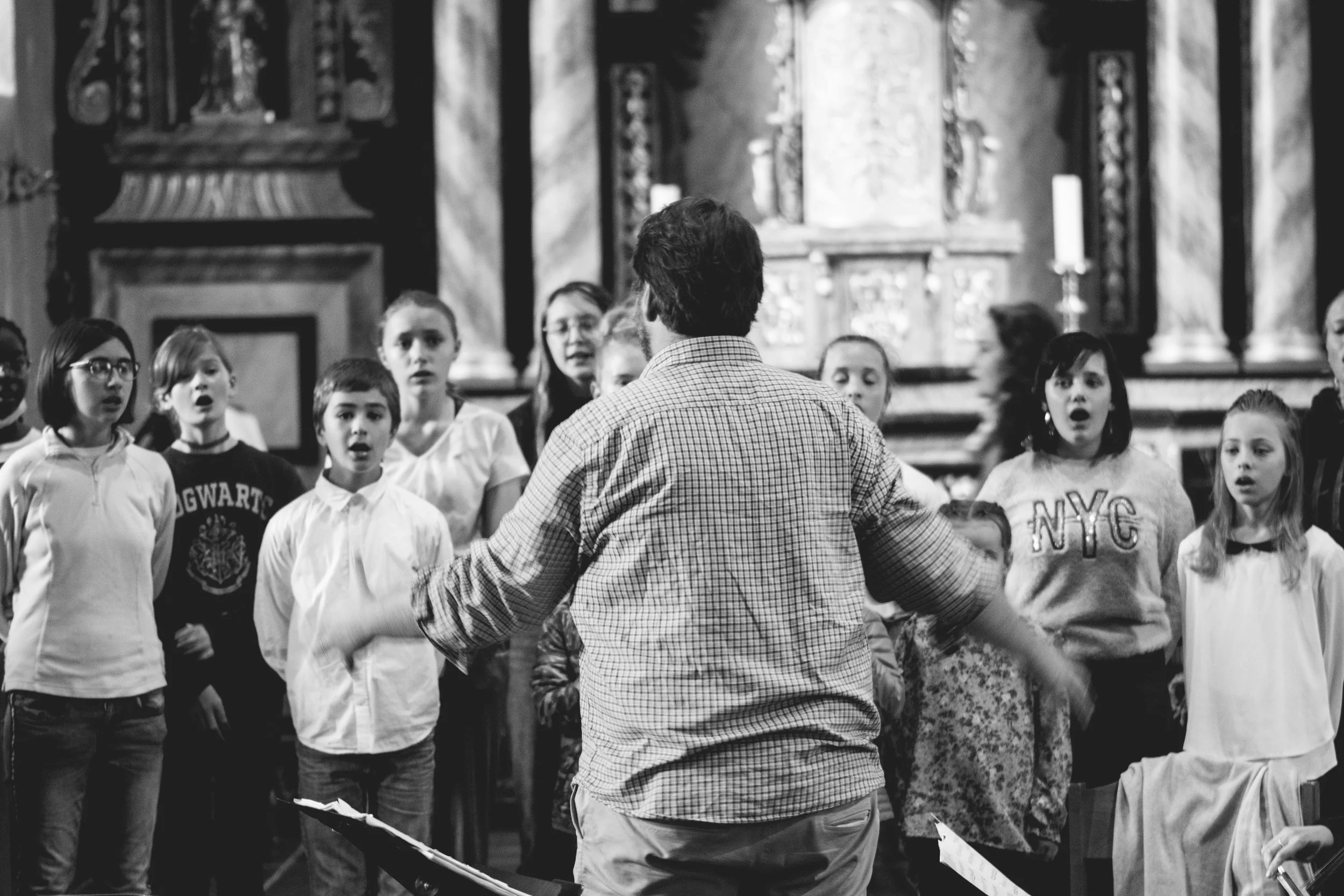 Un groupe d'enfants chantant et un chef d'orchestre dans une église ou une salle de prière, en noir et blanc.