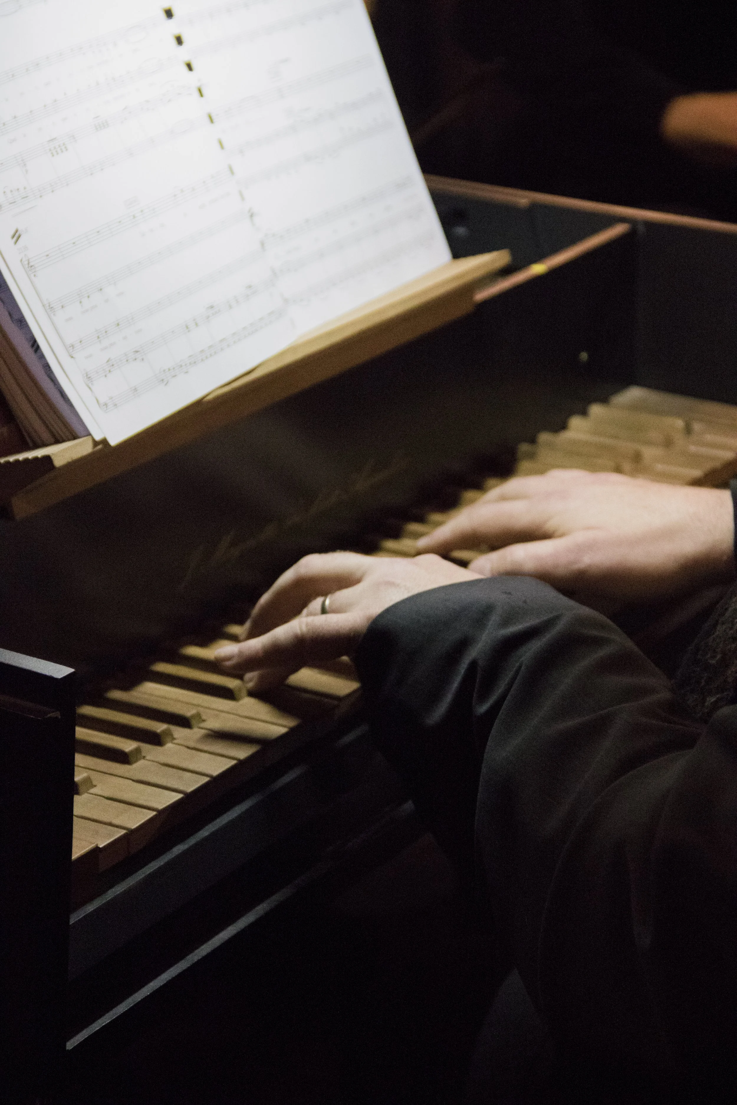 Main d'une personne jouant du piano avec partition musicale ouverte sur le suport. La personne porte un bracelet argenté.