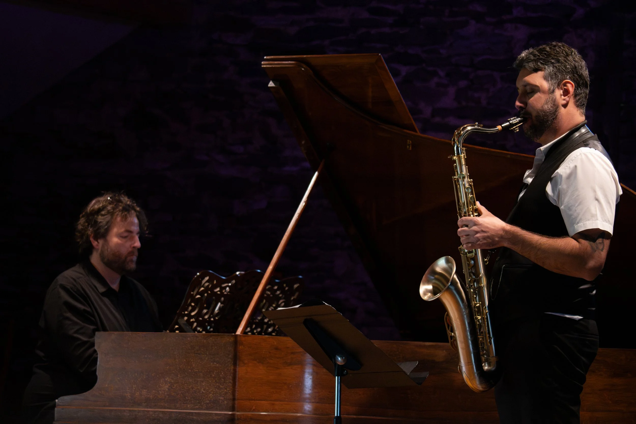 Deux musiciens jouent du piano et du saxophone dans une salle sombre.