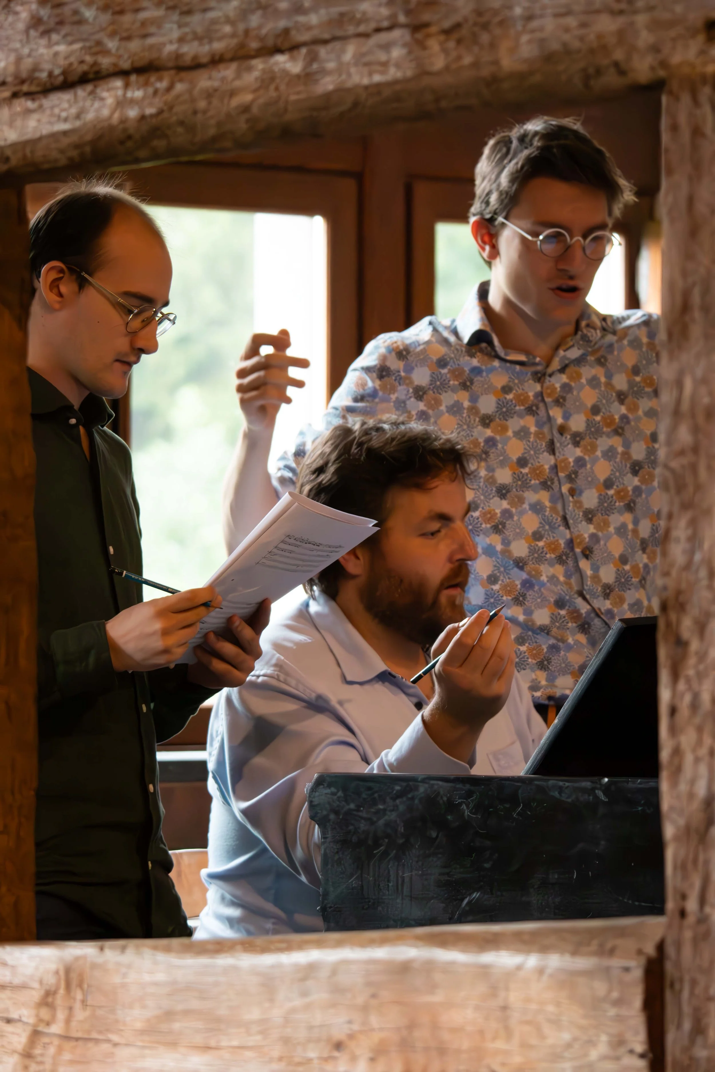Groupe de quatre jeunes musiciens, deux hommes portant des lunettes, jouent du piano dans une pièce avec des fenêtres en arrière-plan.
