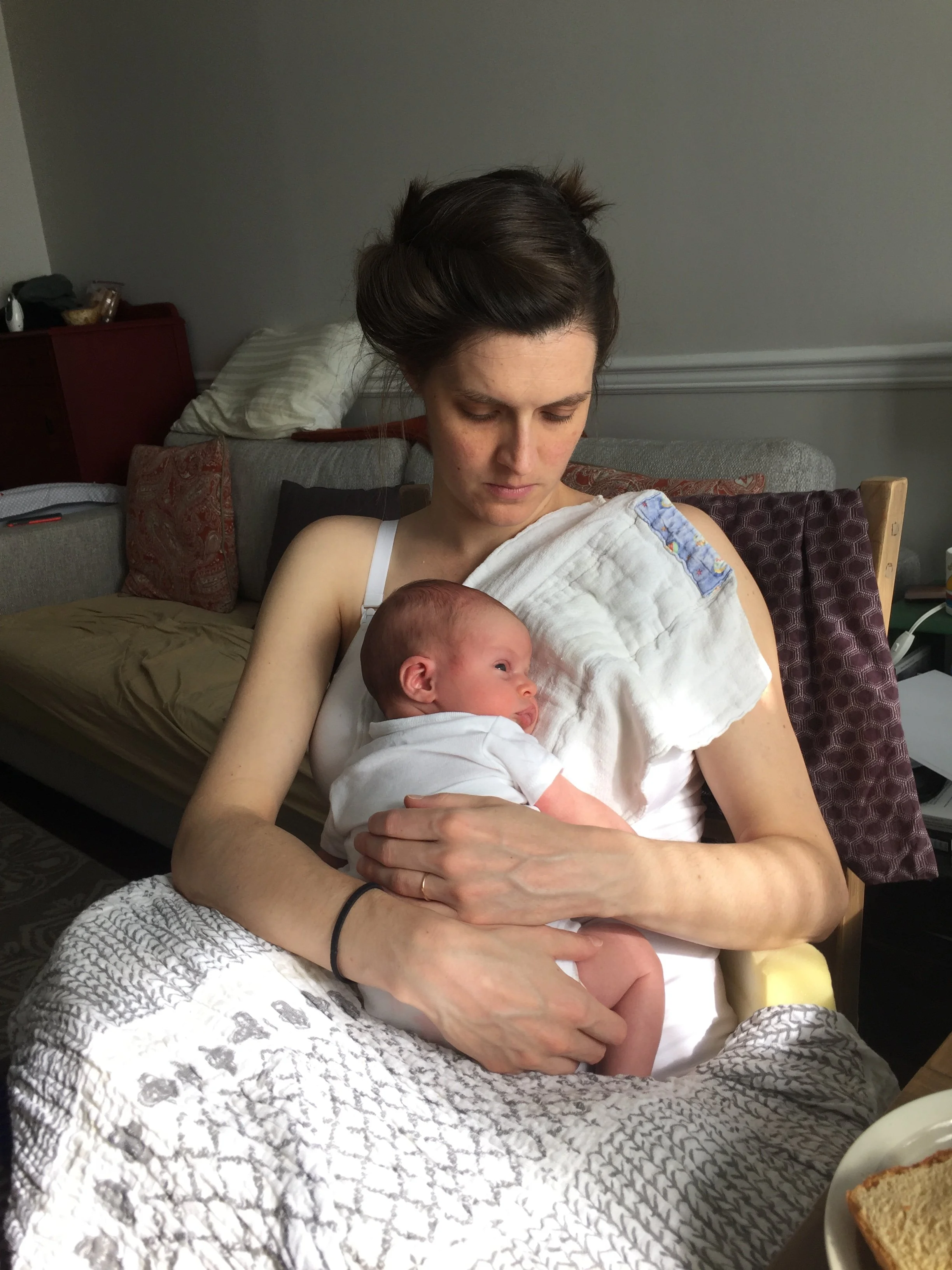 Elissa, sitting on a chair holding a newborn and looking down at the baby.