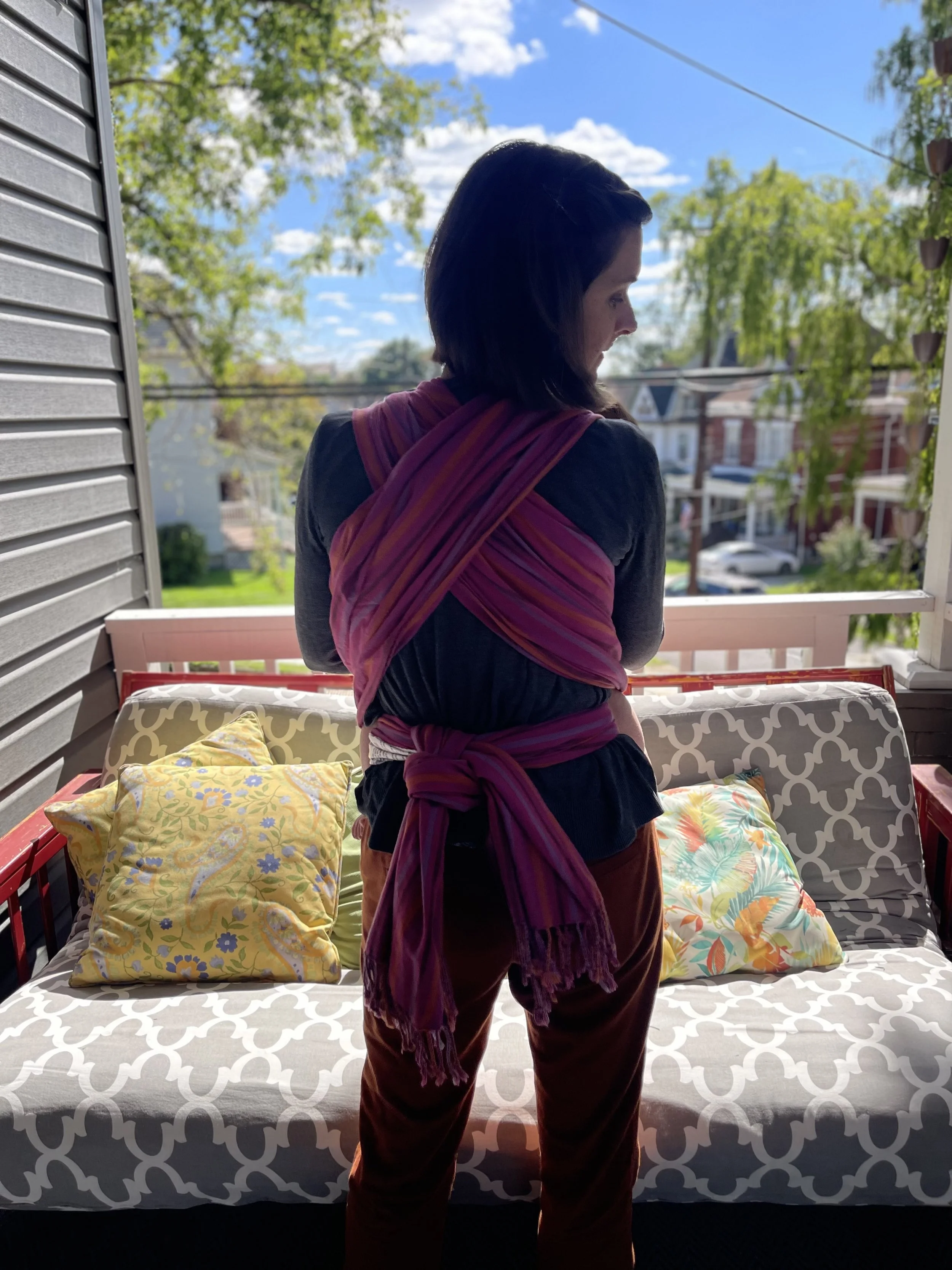 Elissa is standing on a porch with a baby in a fabric carrier on her chest.