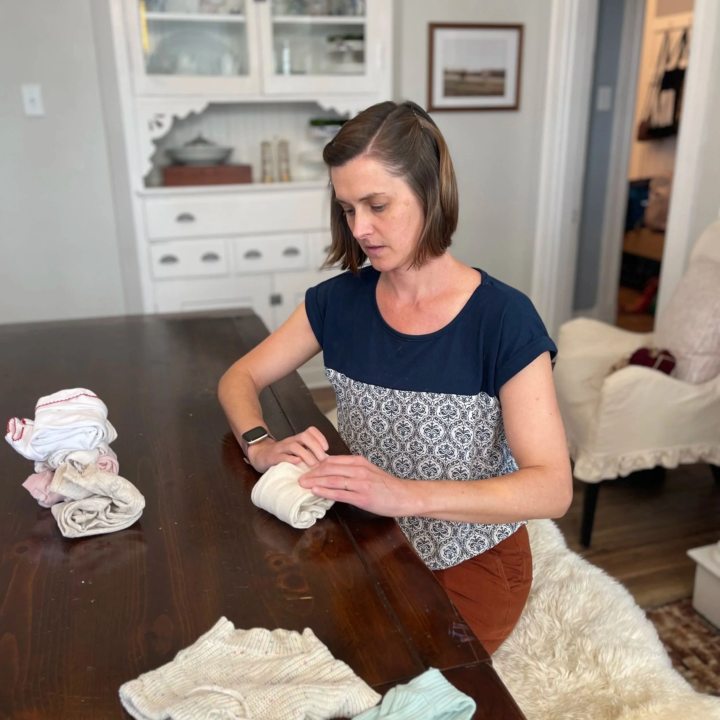 Elissa is seated, folding baby clothes neatly.