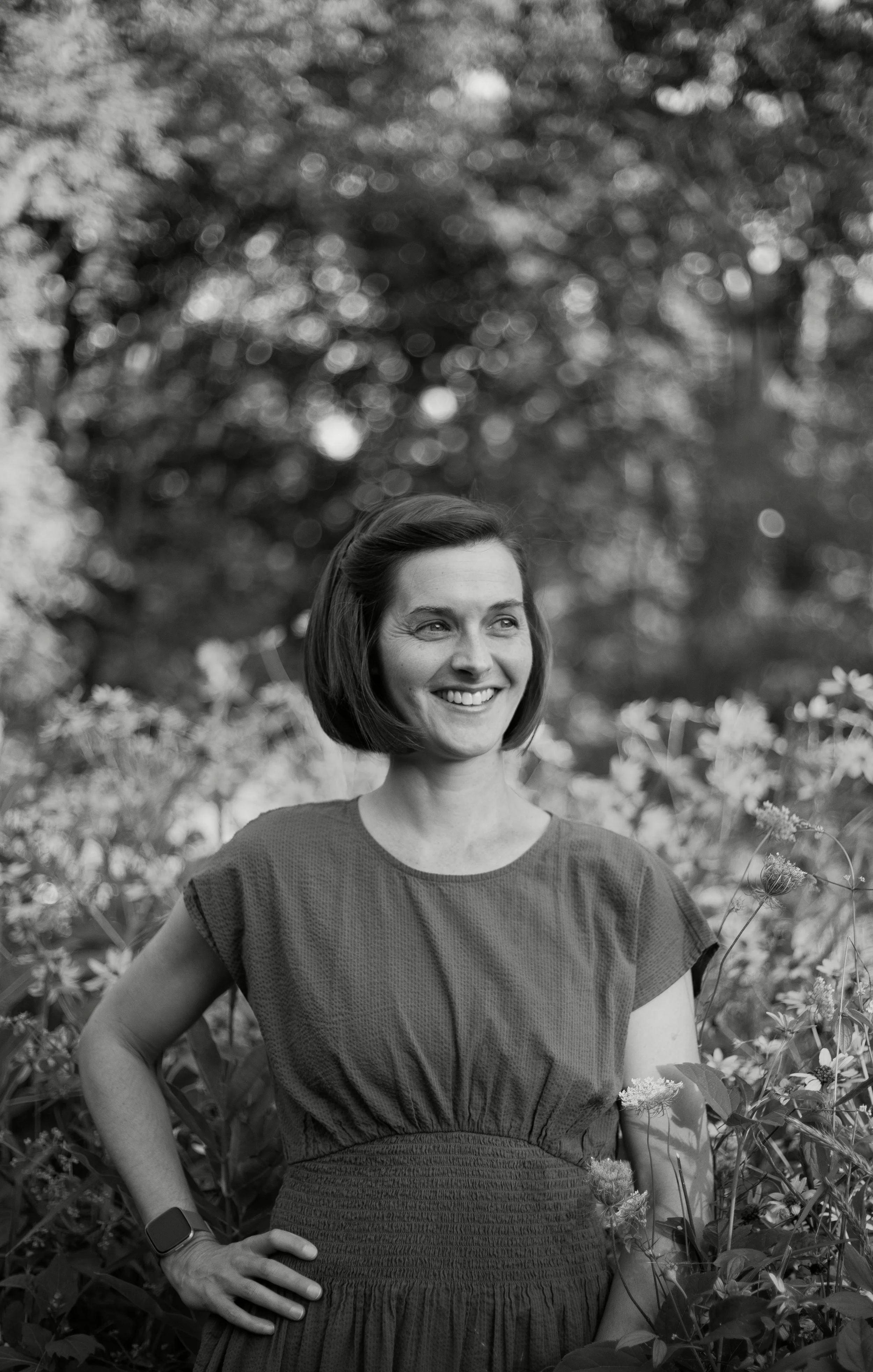A black-and-white photo of Elissa with dark hair standing in front of wildflowers