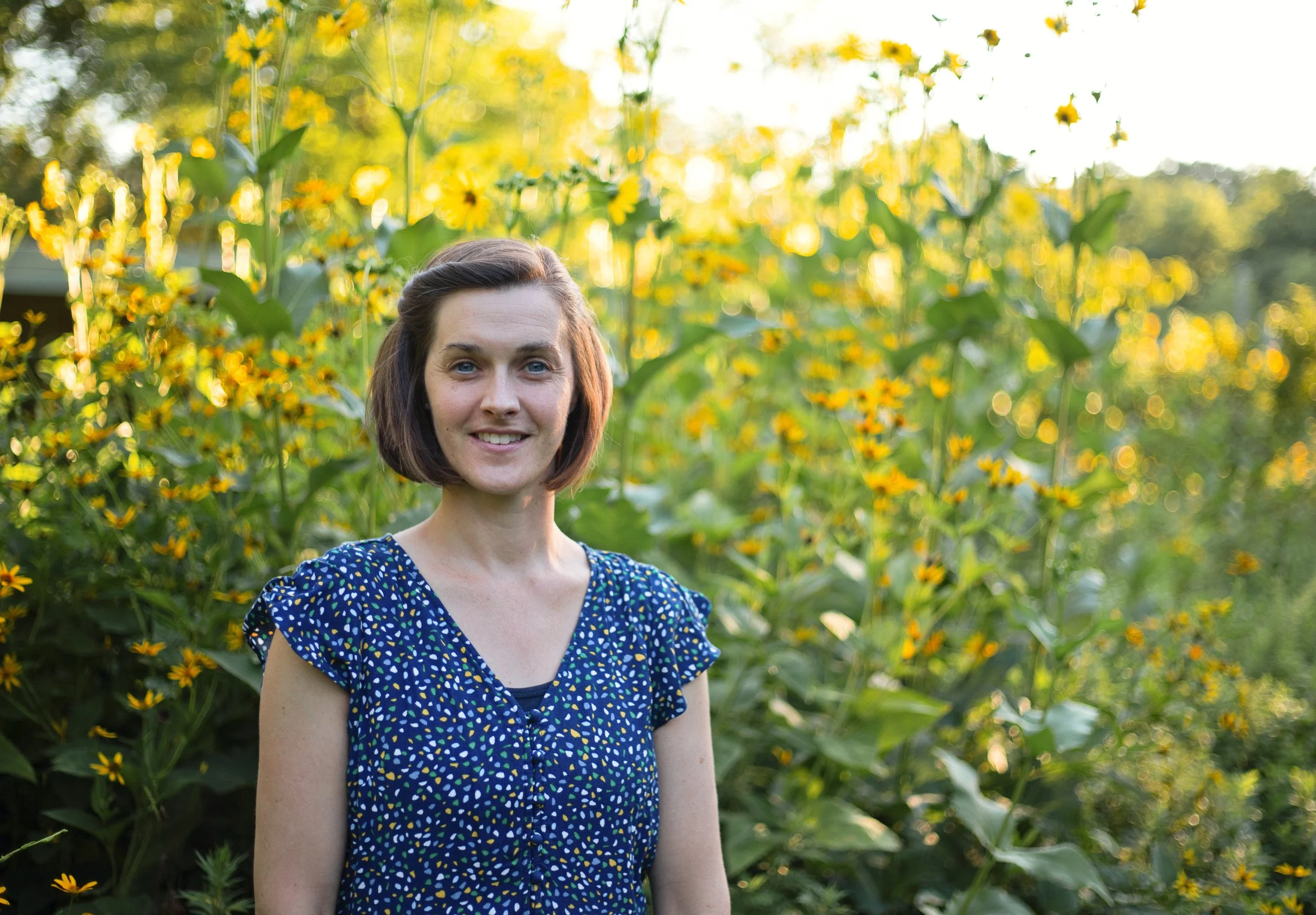 Elissa in a blue dress facing the camera in front of a field of wildflowers.