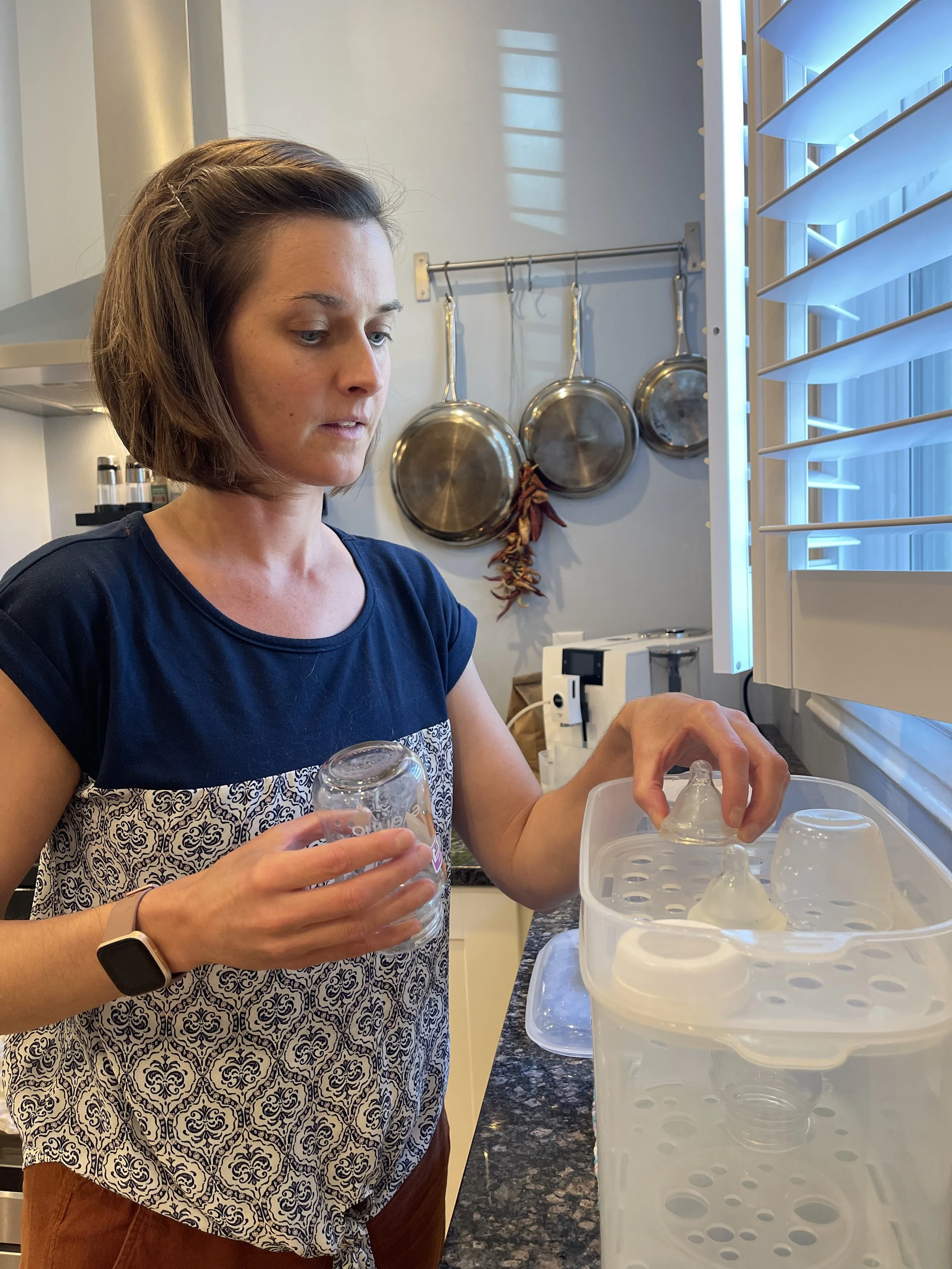 Elissa is in a kitchen filling a bottle sanitizing machine with bottle parts.
