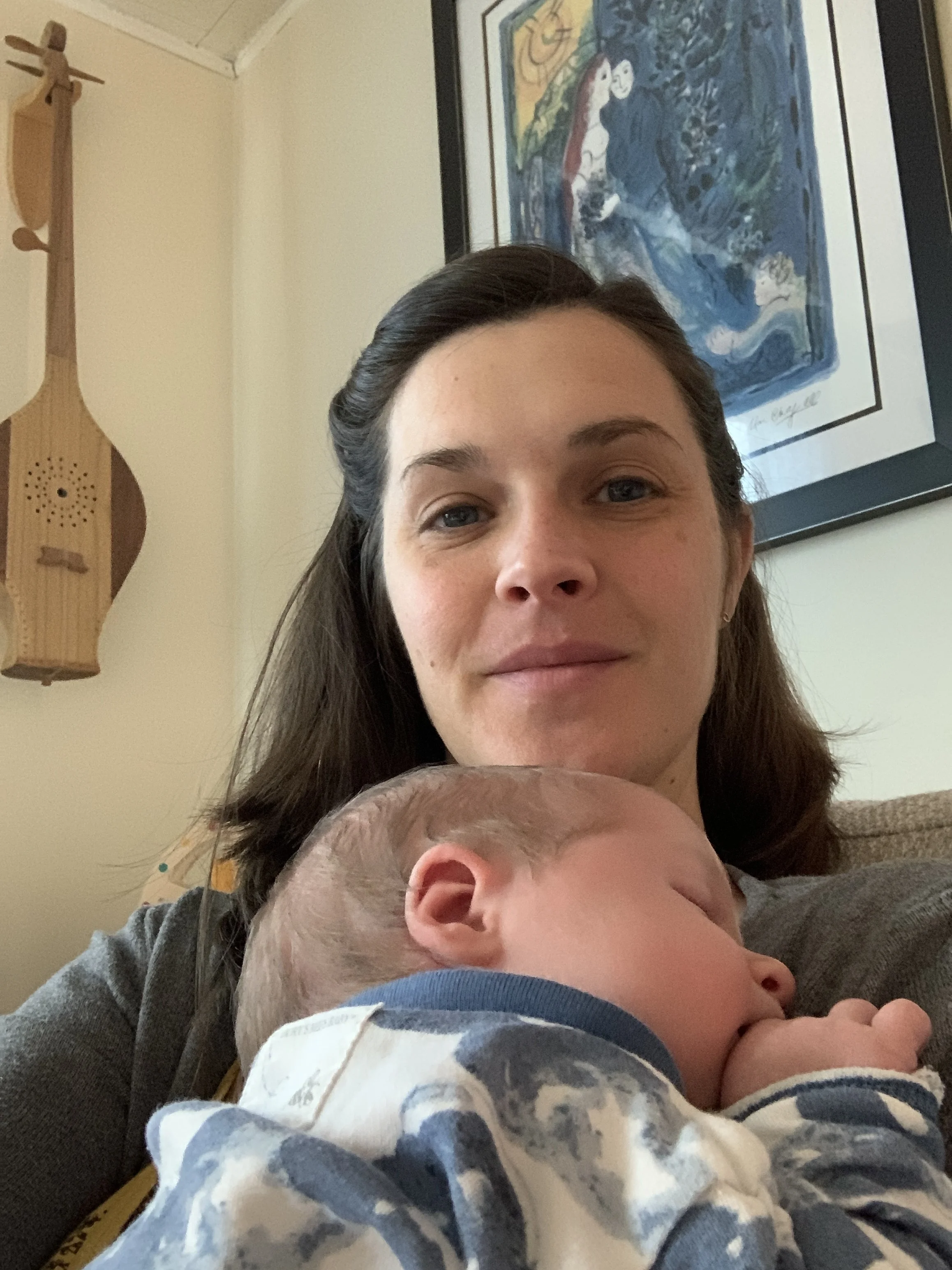 Elissa, sitting and holding a sleeping newborn and smiling.