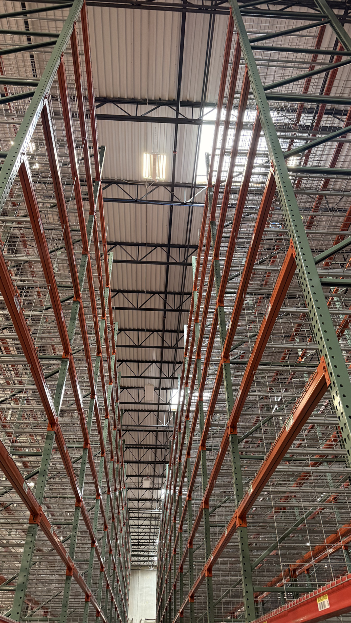 View of empty warehouse shelves with metal racks and orange supports, ceiling with skylights, and high ceiling beams.