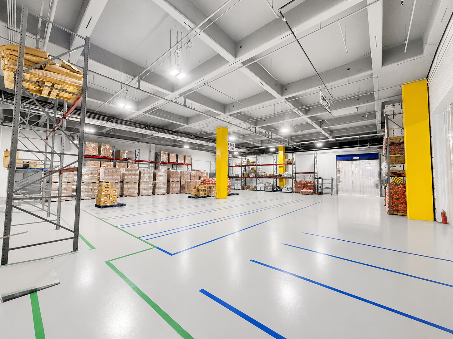 Empty warehouse with storage shelves, pallets of boxed goods, and marked floor areas.