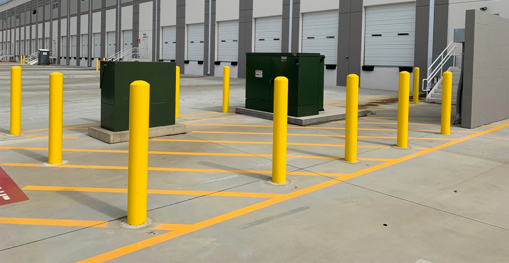 Empty loading dock area with yellow safety posts and two green utility boxes.