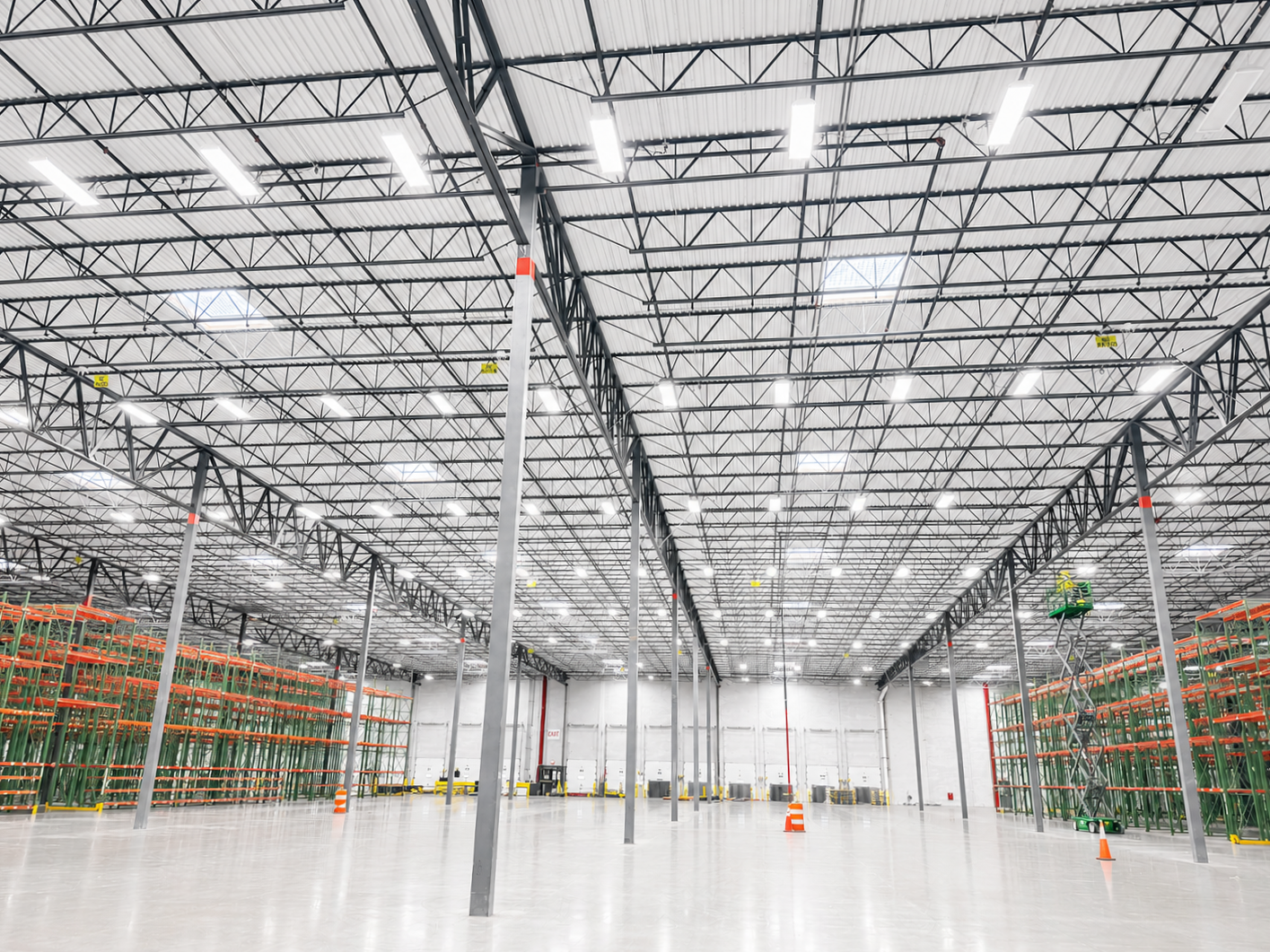 Interior view of a large empty warehouse or distribution center with high ceiling, bright lighting, and shelves on both sides for storing goods.