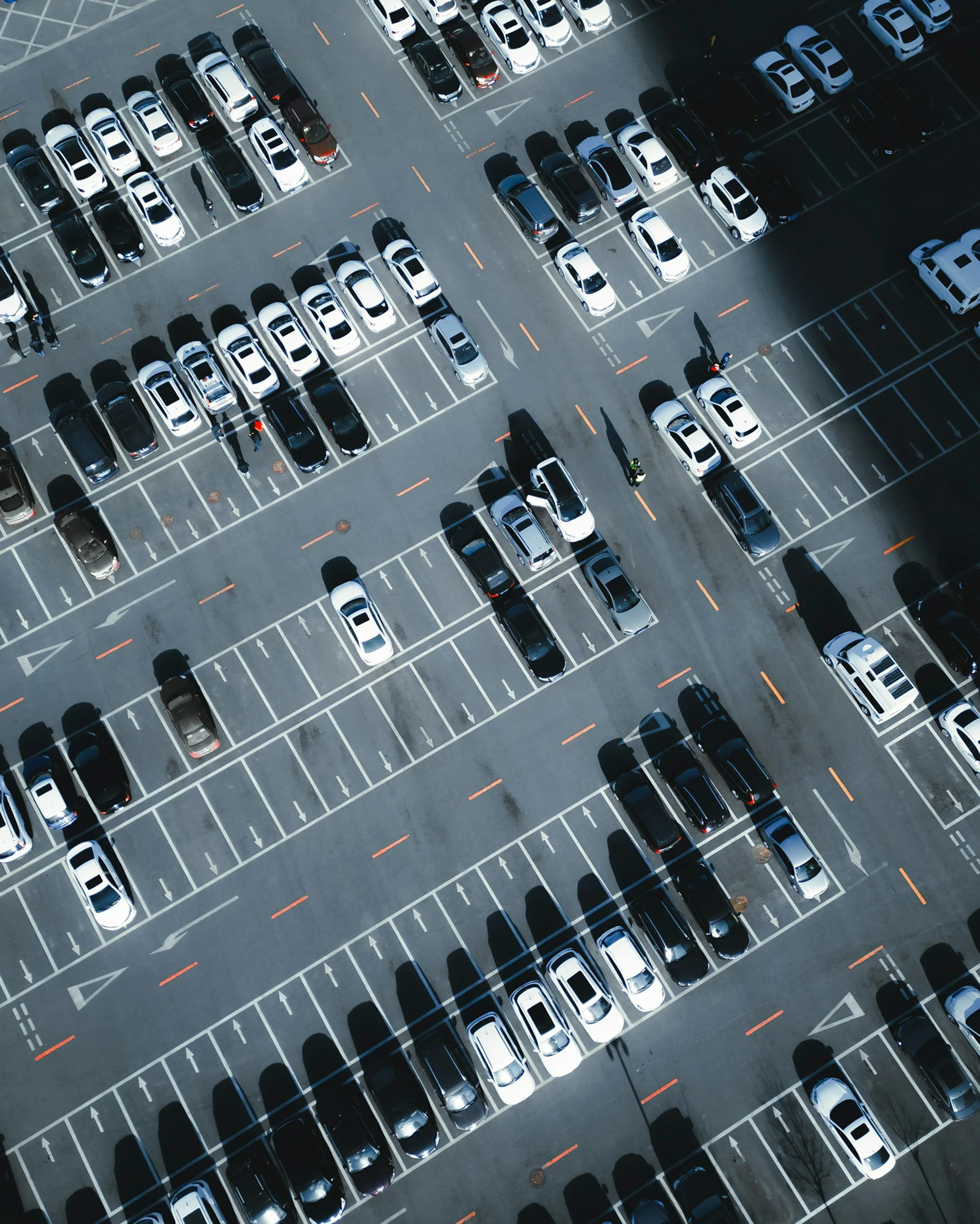 An aerial view of a parking lot filled with white, black, and silver cars parked in marked spaces.