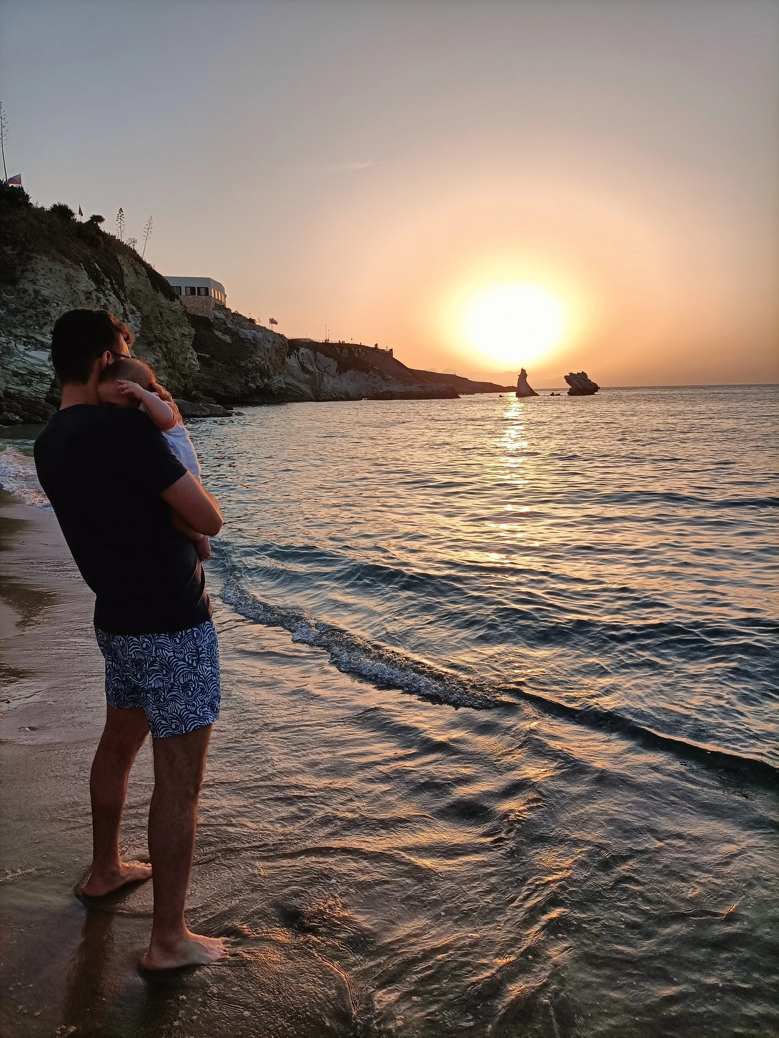 Vito Martino con un bambino in braccio sulla spiaggia al tramonto