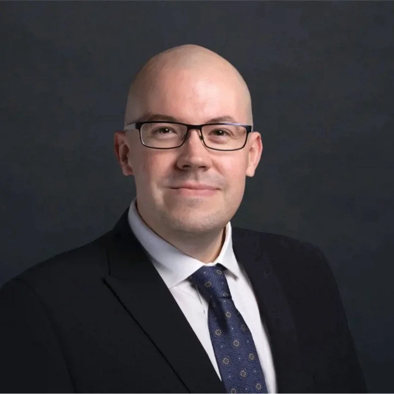 A picture of Scott Vanes who is a Solicitor in Bromyard, Herefordshire. The photo shows a man with glasses, dressed in a suit and tie, posing against a dark background.