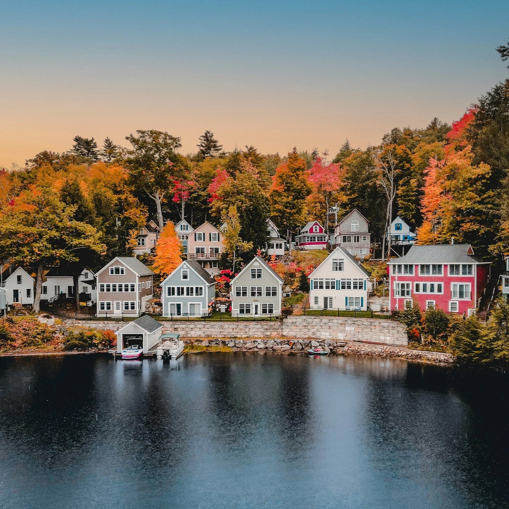 Colorful houses on a hill by the water with trees showing fall foliage in the background.