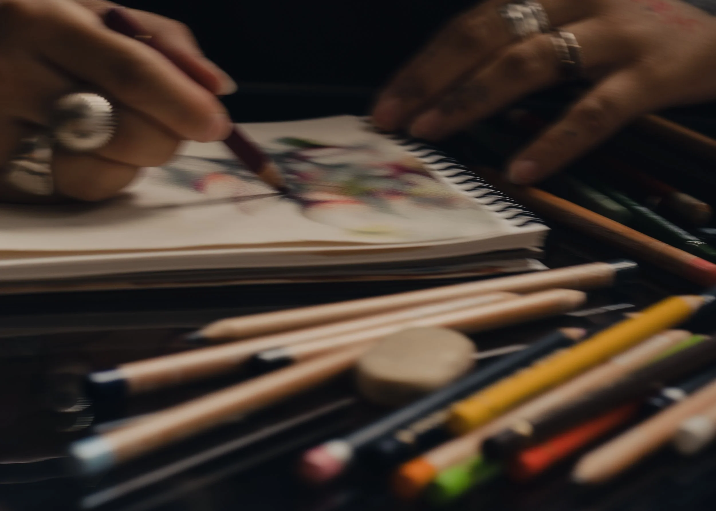 Main dans un carnet de croquis, utilisation de crayons de couleur pour réaliser un dessin coloré, avec des crayons de couleur alignés au premier plan