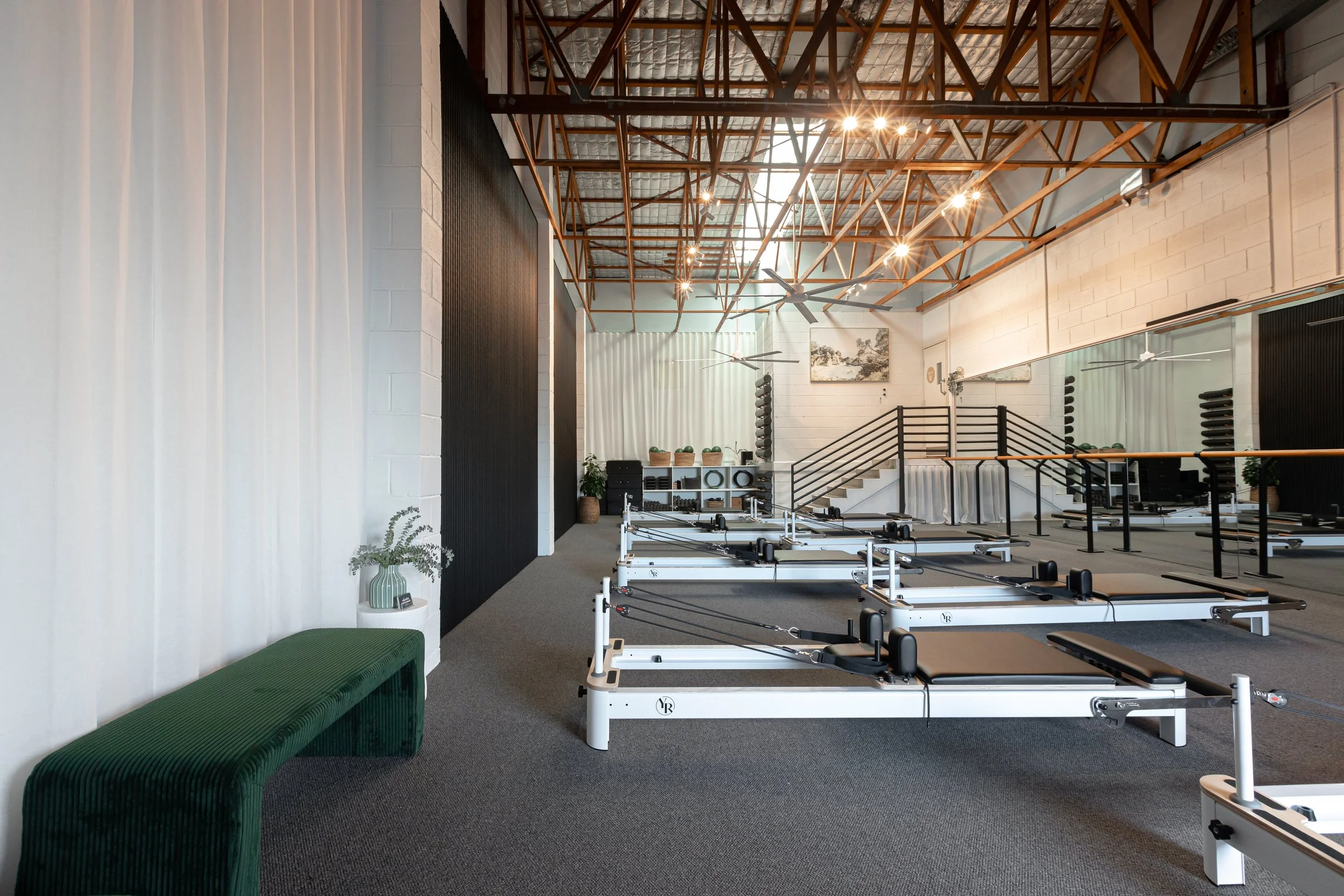 The Interior of Mindful Movement Pilates Studio with Reformers, mirrors, ceiling fans, illuminated by ceiling lights and natural light.