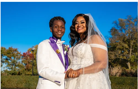 Bride and groom posing outdoors on their wedding day, with the groom wearing a white suit and purple lapel trimming and bow tie.