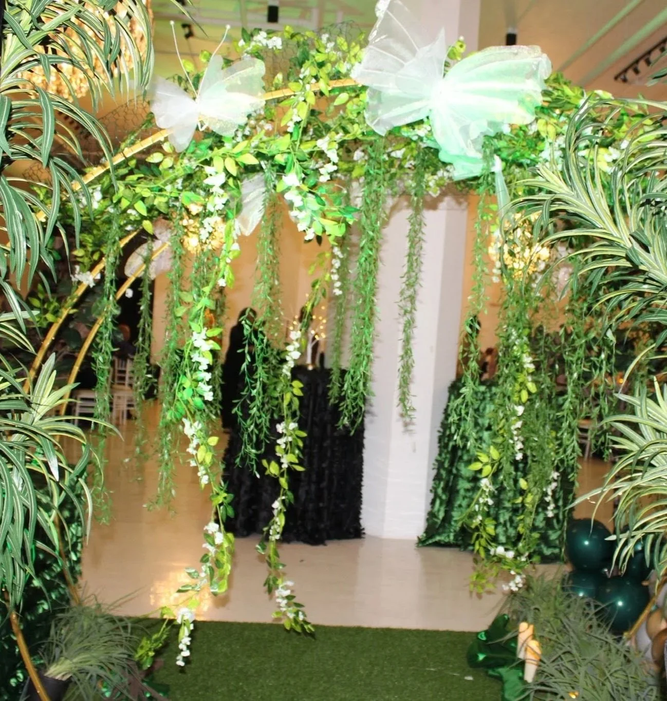Event entrance decorated with lush greenery, hanging white flowers, and butterfly accents.