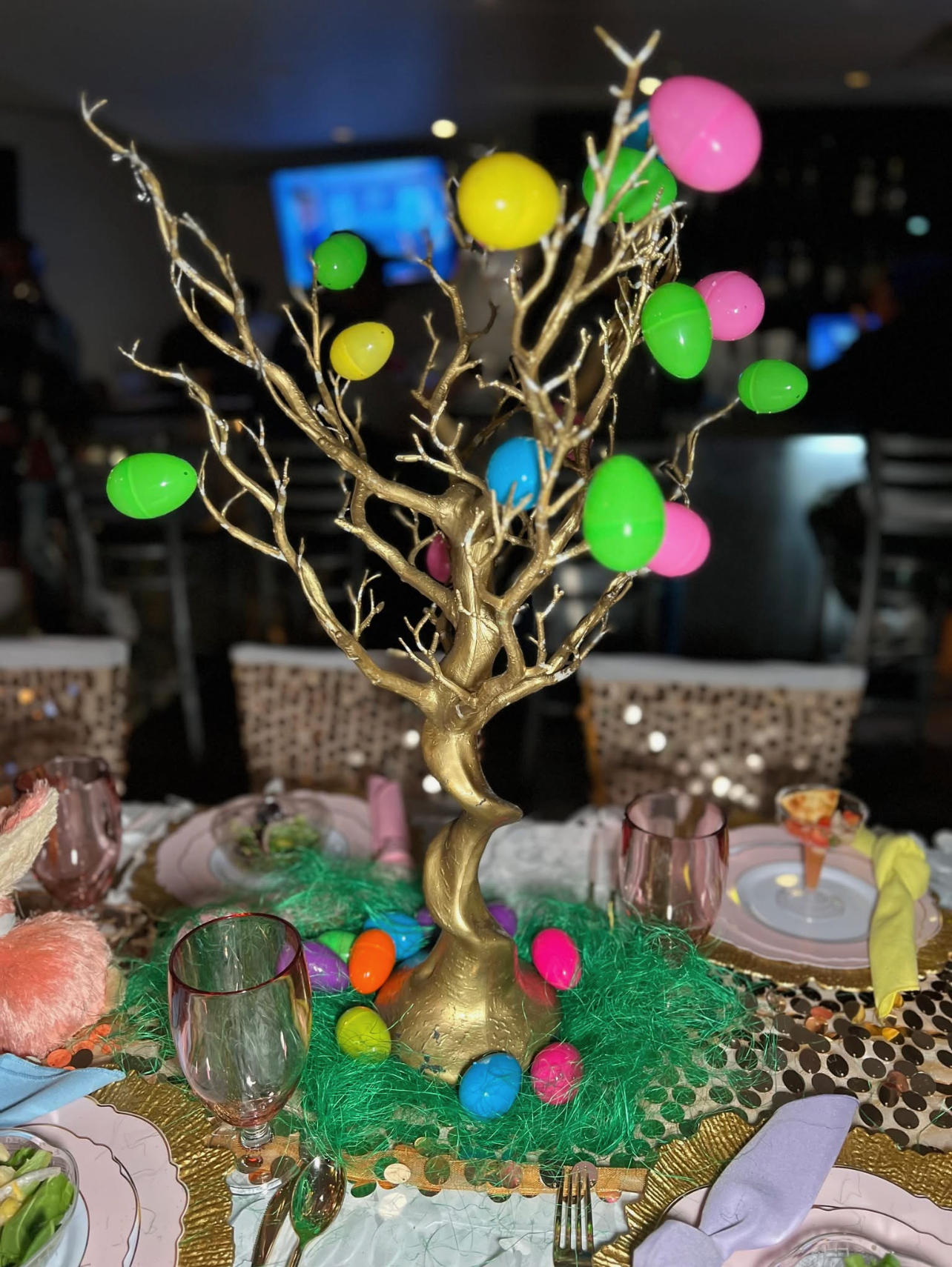 Gold Easter tree centerpiece decorated with colorful eggs on a celebration table.