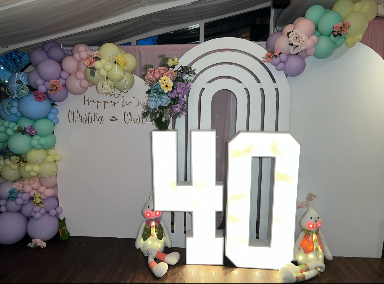 Pastel 40th birthday display with an illuminated "40" sign, balloons, flowers, and plush rabbits.