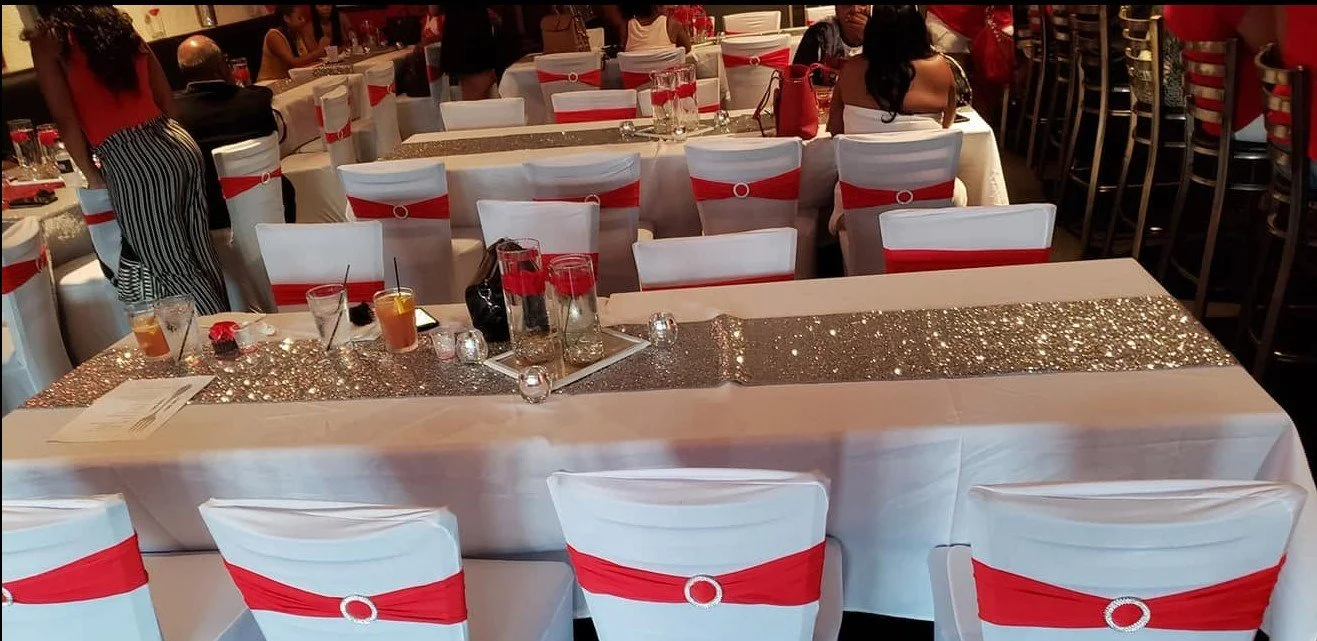 Formal banquet tables with white linens, sparkling accents, and white chair covers with red sashes.
