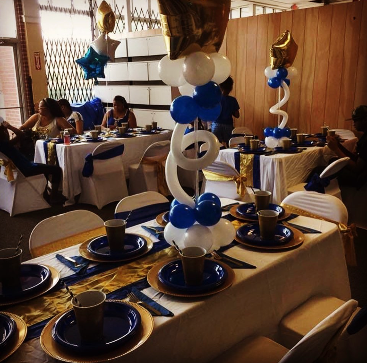Blue, white, and gold banquet hall setup with balloons and coordinated table settings.