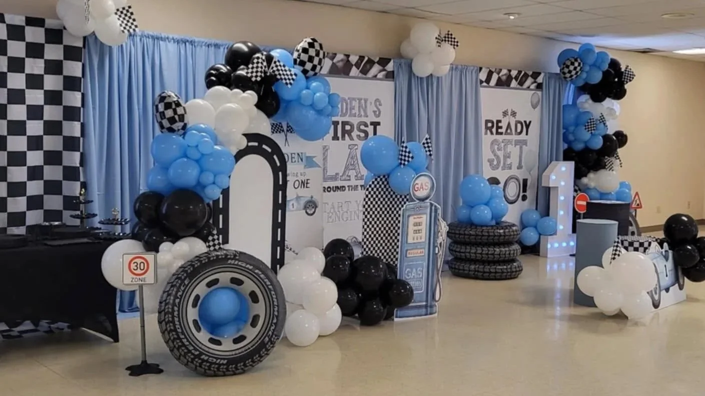 Blue, black, and white race-car birthday setup with balloons, checkered flags, tires, and themed decorations.