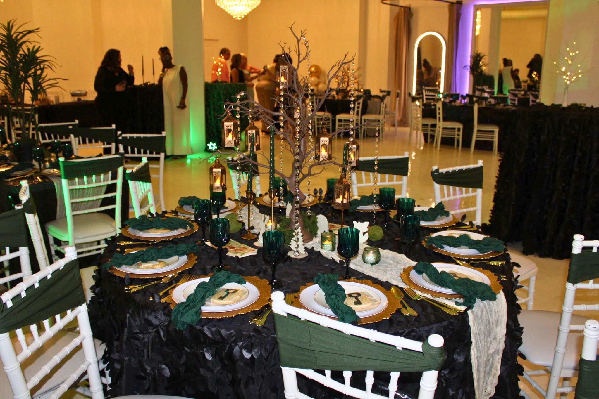 Black-and-gold banquet table with gold chargers, green napkins, black glassware, and a decorated centerpiece tree.