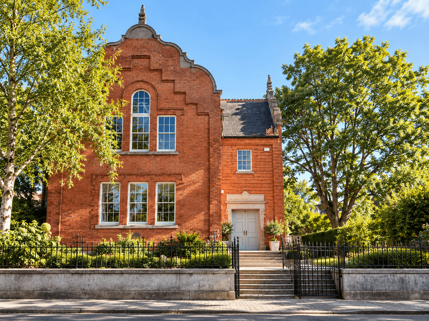 Large red brick building with trees surrounding and blue sky.