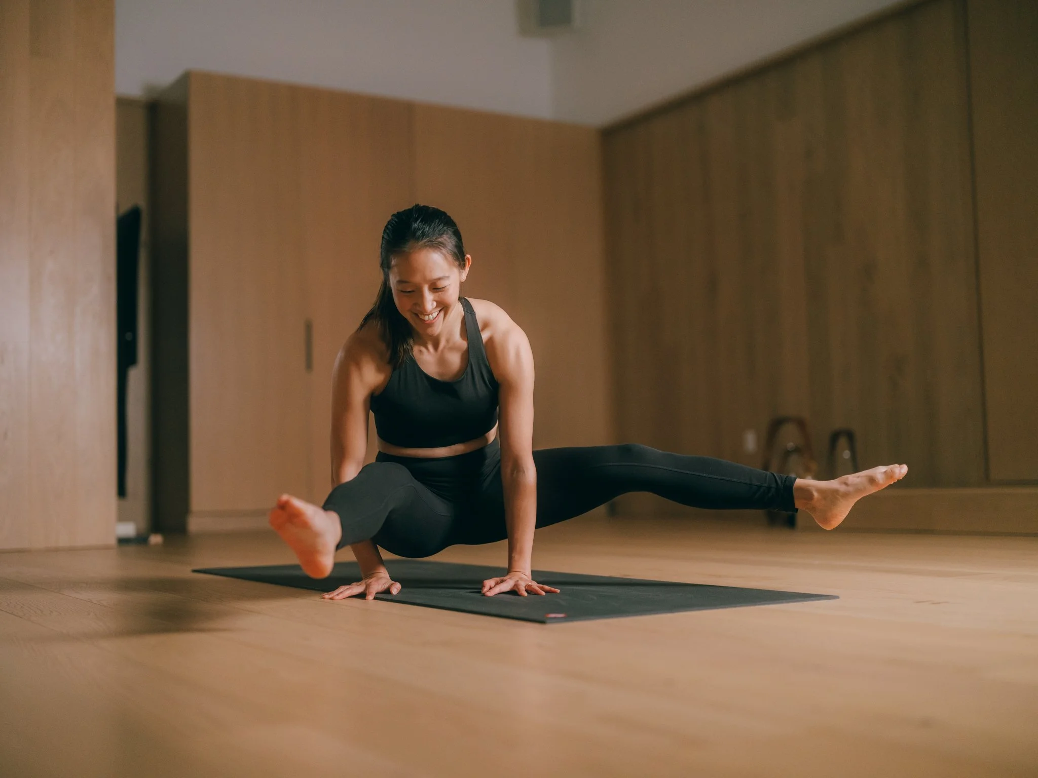 A woman practicing yoga in a studio, balancing on her hands with her legs extended in a split position.