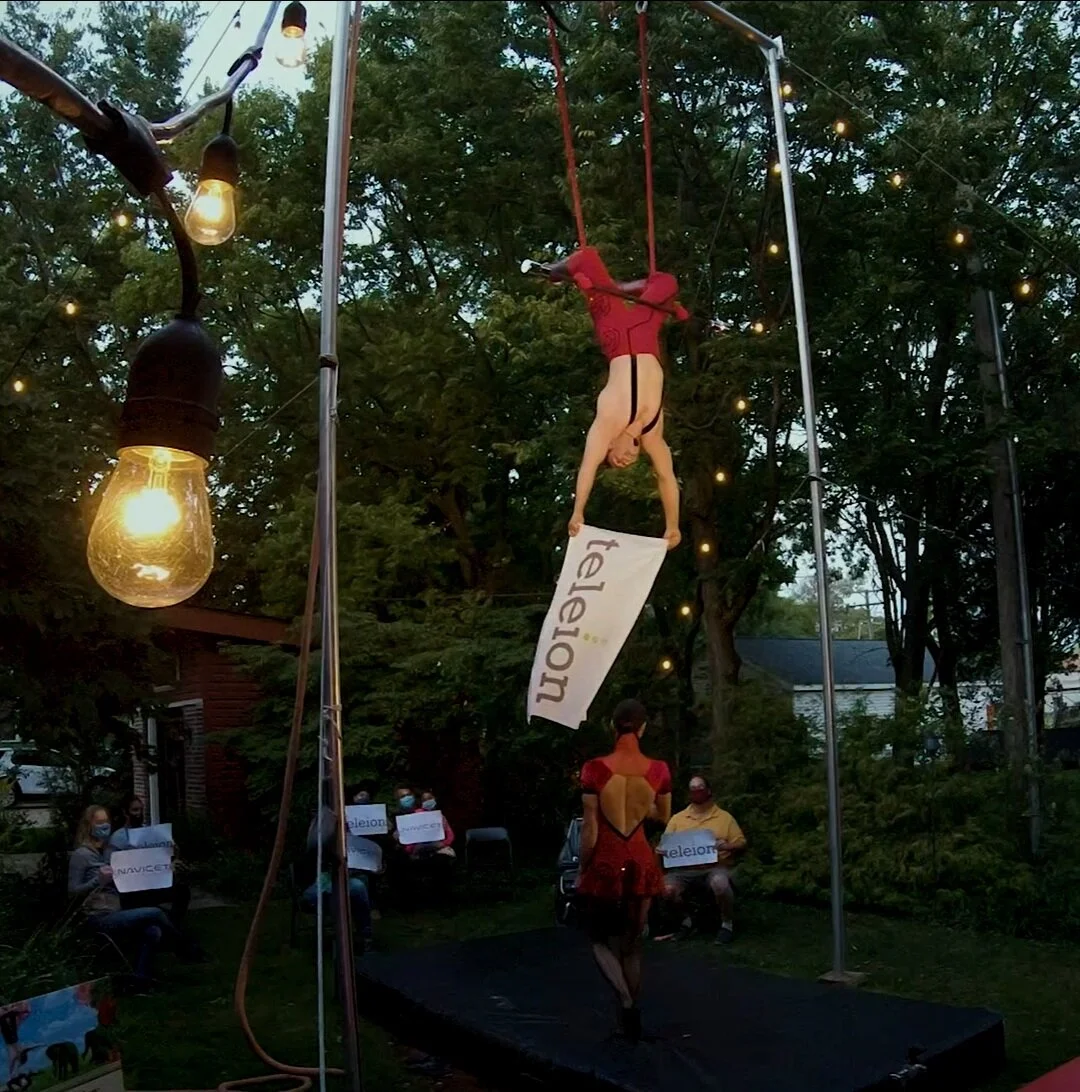 Duo Rose uses a 4 foot canvas sign to lift onto the Trapeze while backyard circus attendees hold up signs