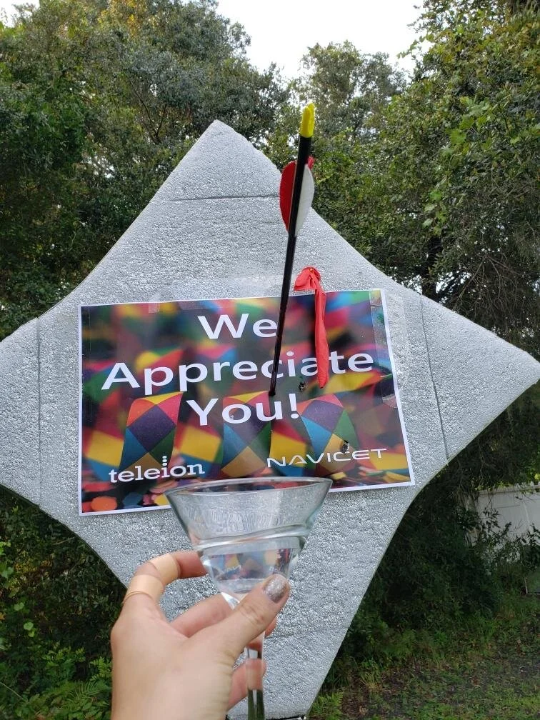Elayne Kramer shoots a 12 inch balloon with an arrow to reveal a “We Appreciate You!” sign on her target