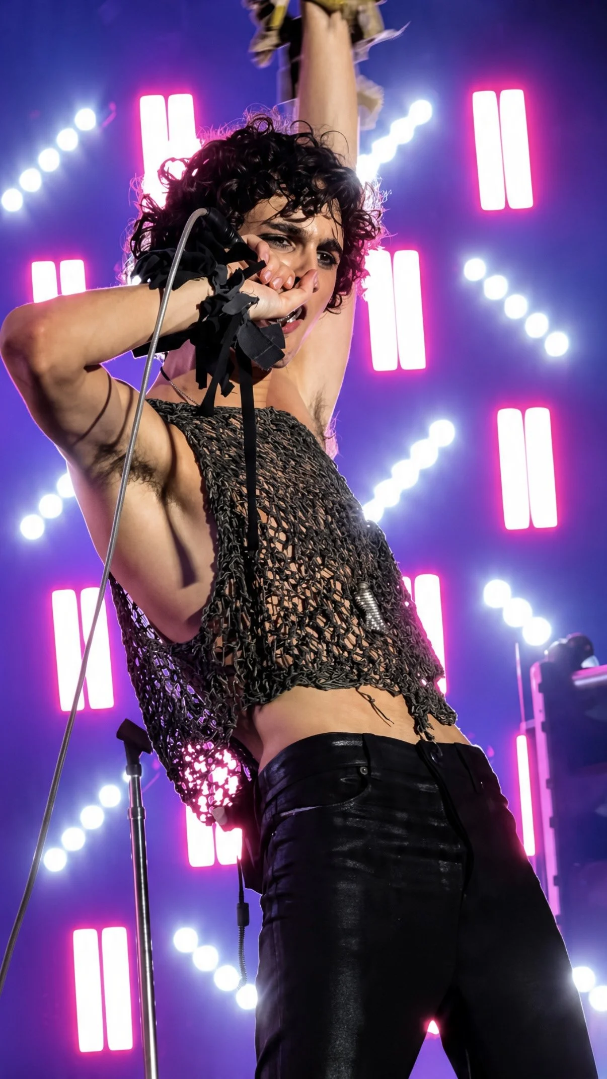 Sombr performing with one arm raised under pink and white stage lights.