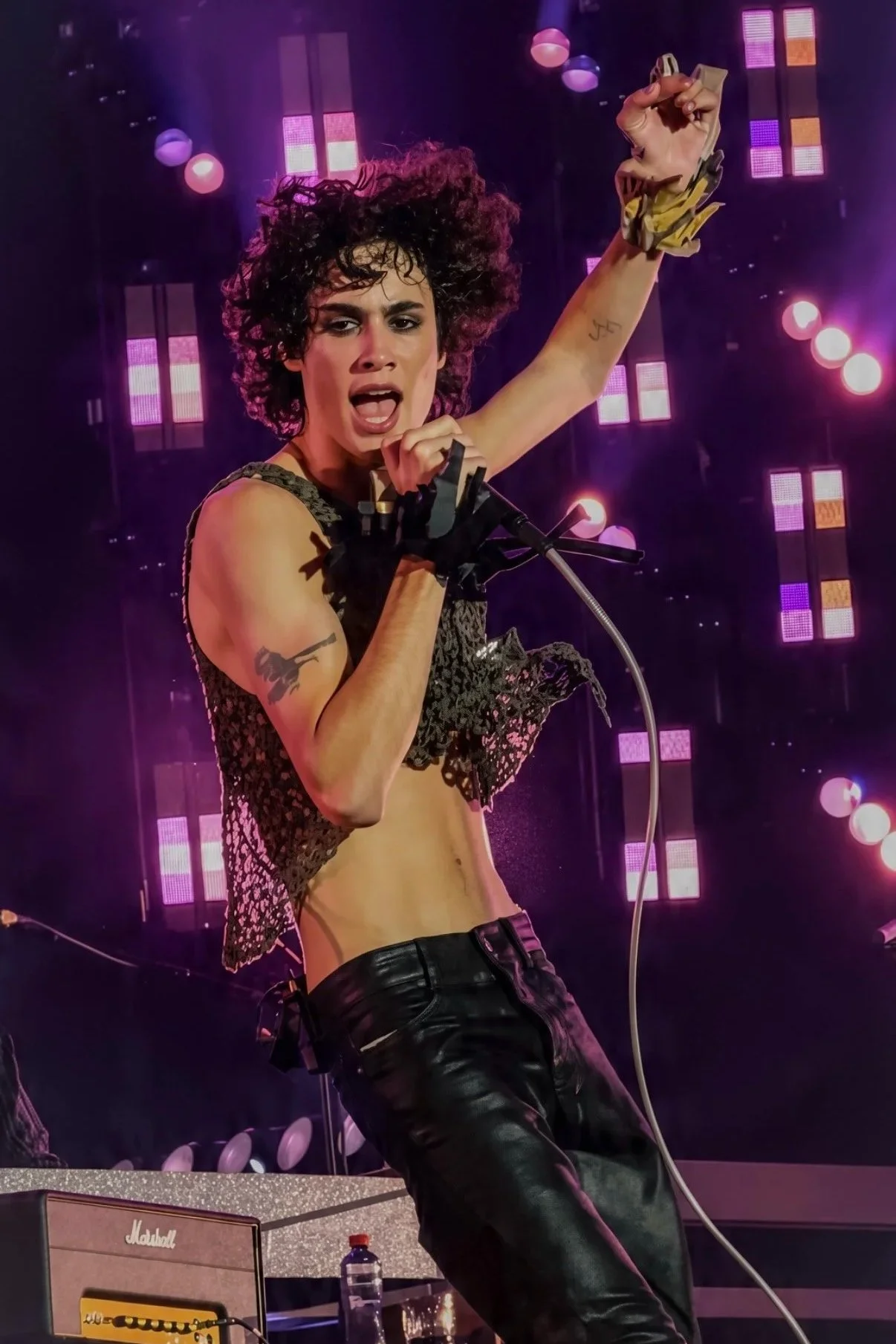 Sombr performing with one arm raised against purple stage lighting.