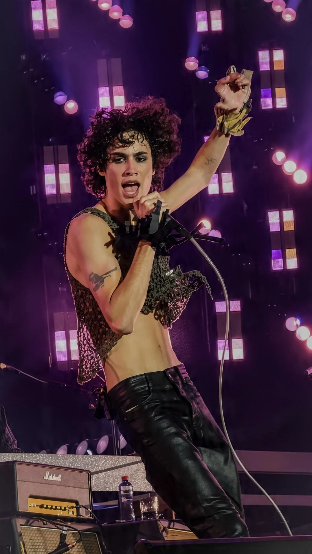 Sombr performing with one arm raised against purple stage lighting.