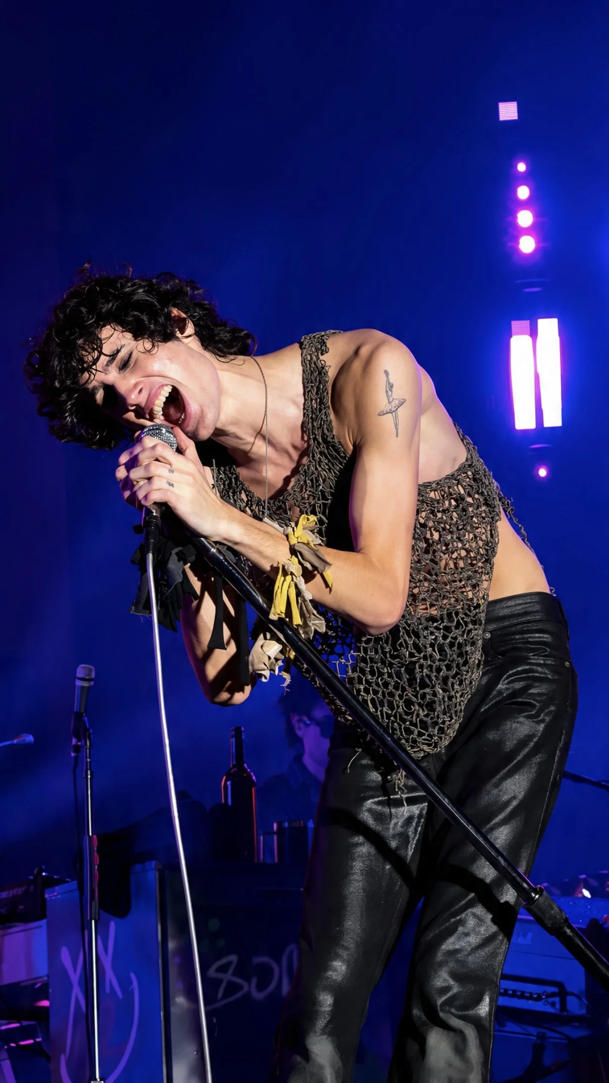 Sombr leaning into the microphone during a live performance under blue stage lights.
