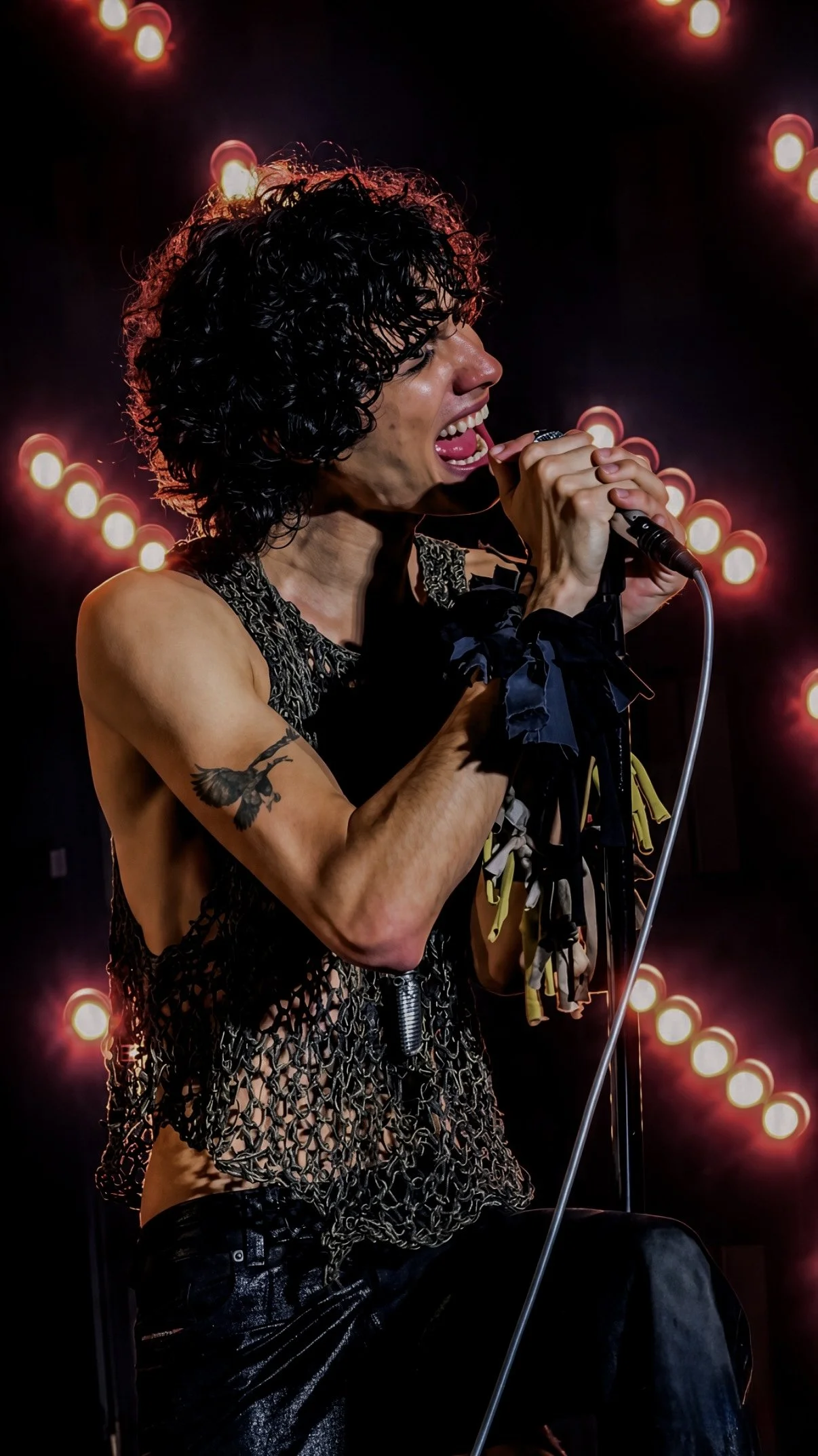 Sombr singing into a microphone in profile with warm red stage lights behind him.